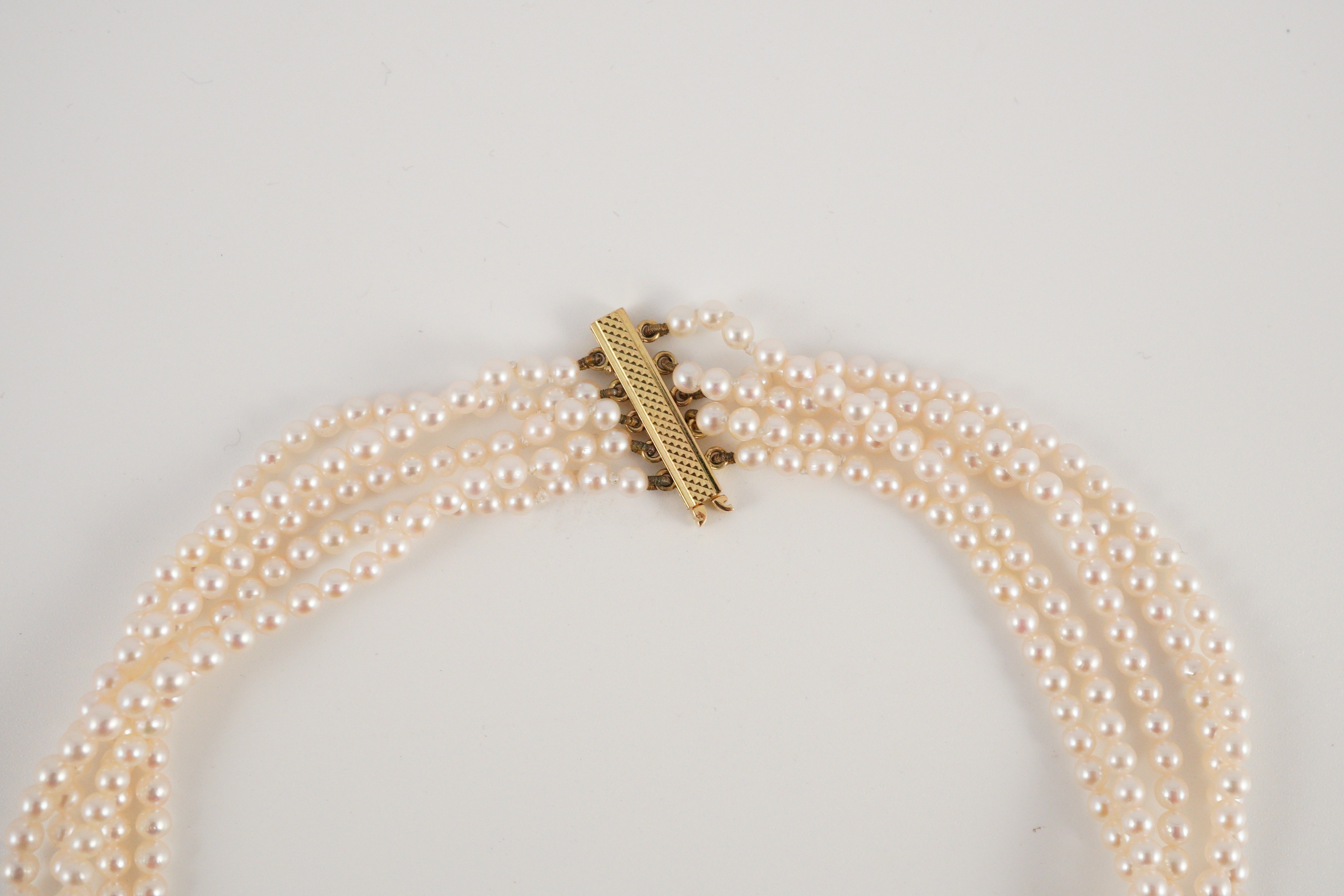 A quintuple strand seed pearl choker necklace, with pierced gold, platinum and diamond cluster set quatrefoil shaped clasp